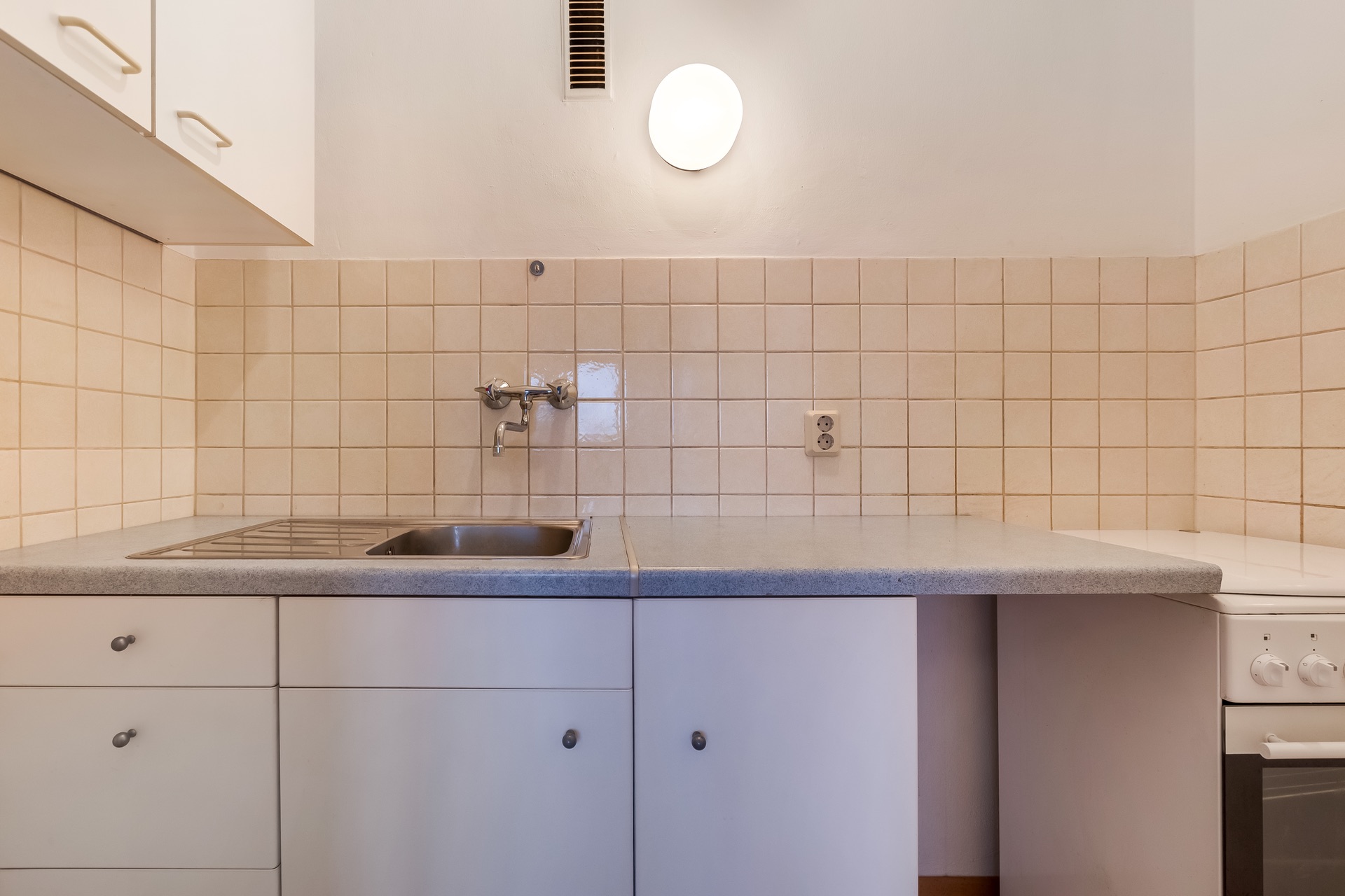 Moderne Küchenzeile mit Spüle, Herd, Hängeschränken und beige Fliesenwand.