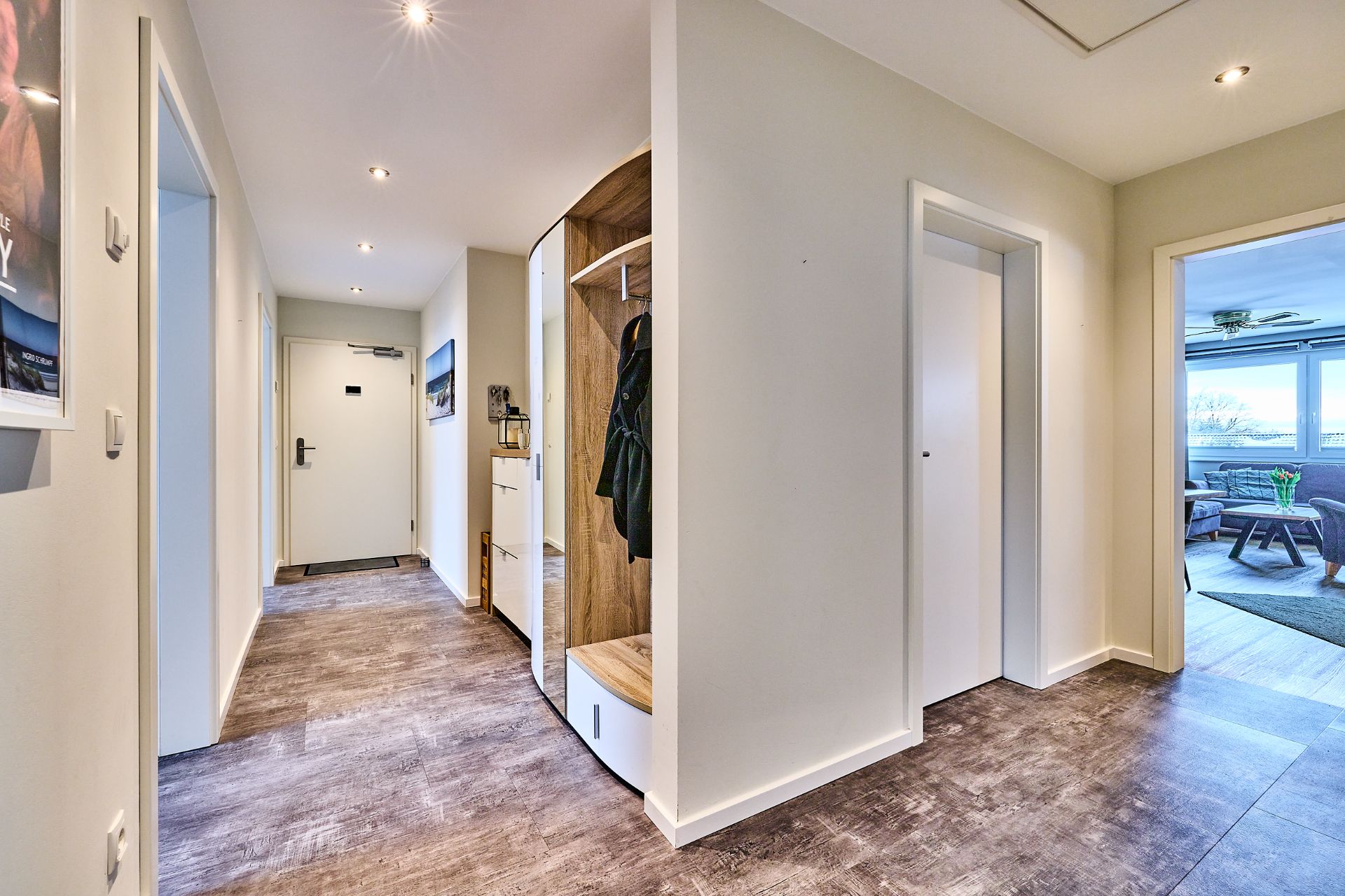 Moderner Flur mit Garderobe, weißen Türen und Blick in ein Wohnzimmer mit großen Fenstern.