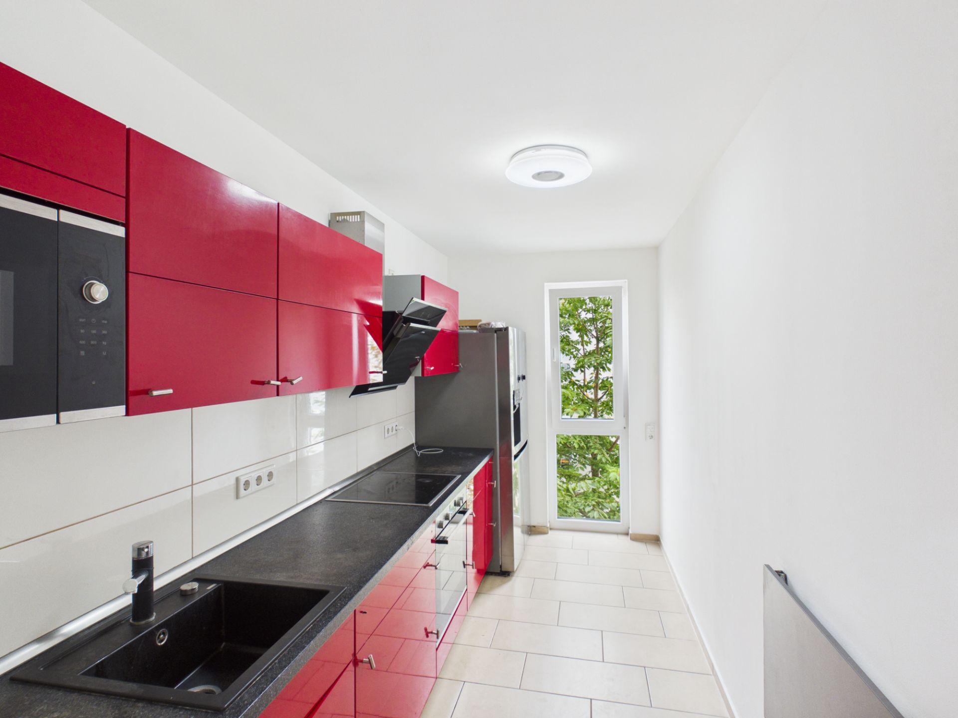 Moderne Küche mit roten Schränken, schwarzen Arbeitsflächen und großem Fenster.