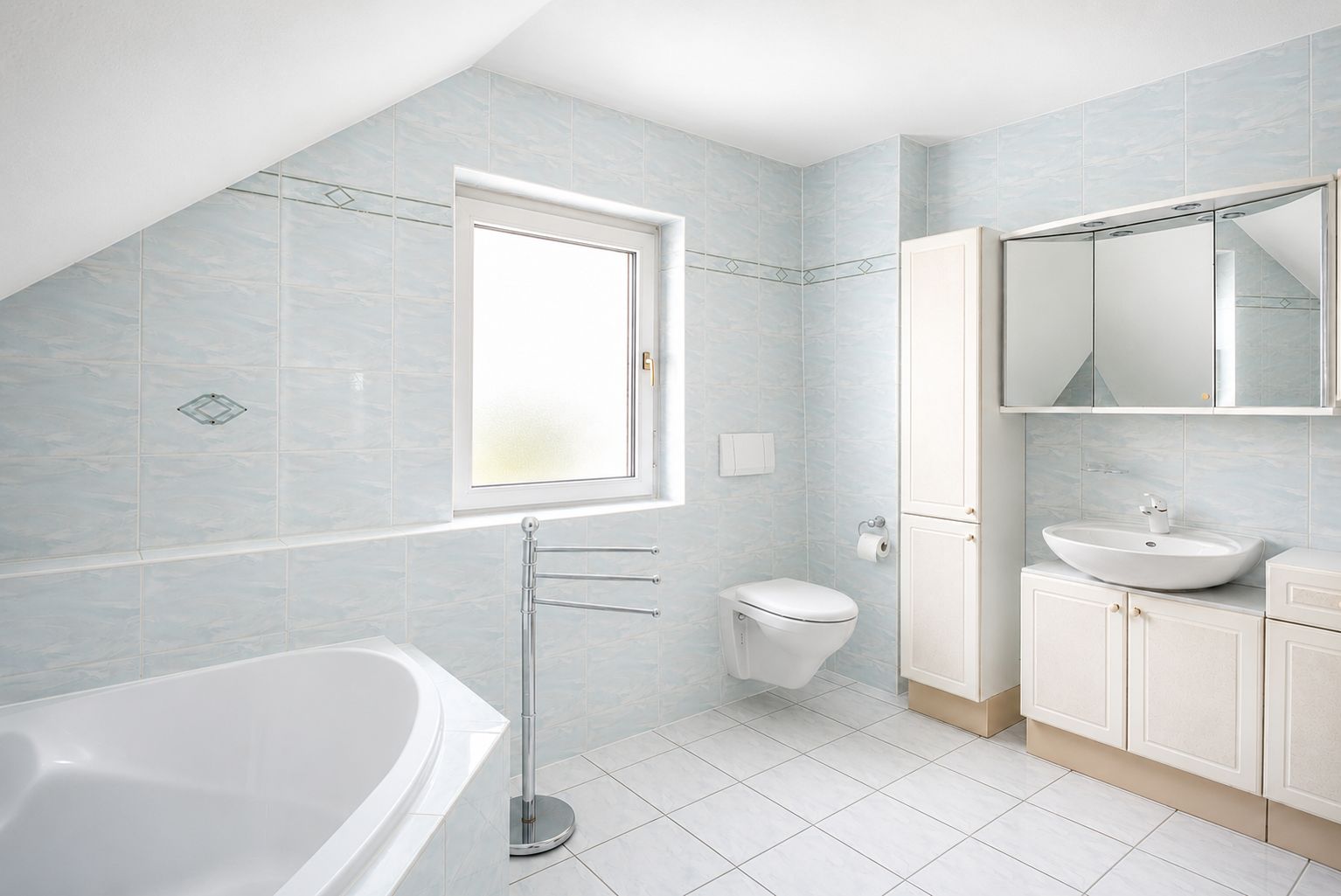 Helles Badezimmer mit Badewanne, Wandtoilette, Waschbecken, Spiegel und Fenster.