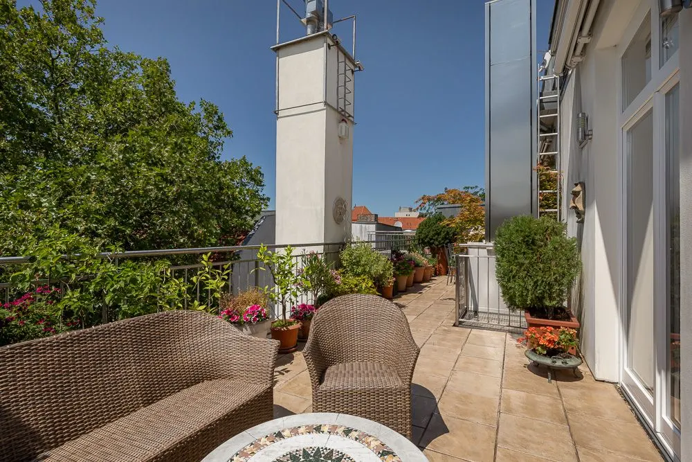 Sitzbereich mit Korbmöbeln und vielen Blumentöpfen auf einer sonnigen Terrasse.