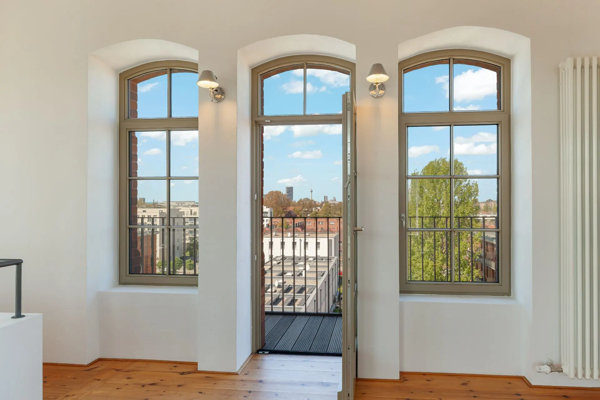 Drei große Fenster und eine geöffnete Tür führen auf einen kleinen Balkon mit Stadtblick.