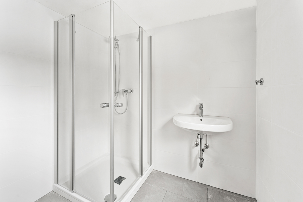Modernes Bad mit Glasdusche und Waschbecken vor weißen Fliesenwänden.