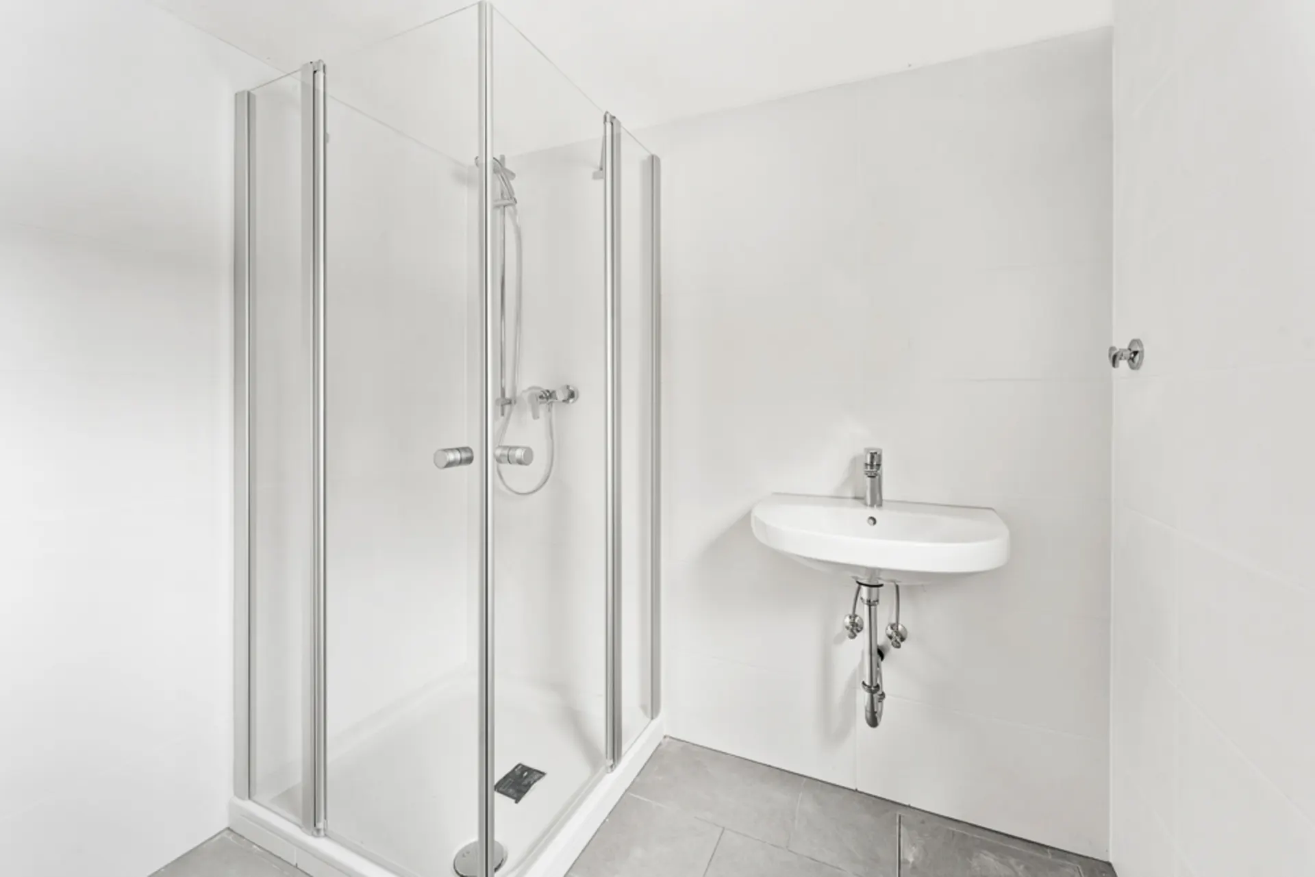 Modernes Bad mit Glasdusche und Waschbecken vor weißen Fliesenwänden.