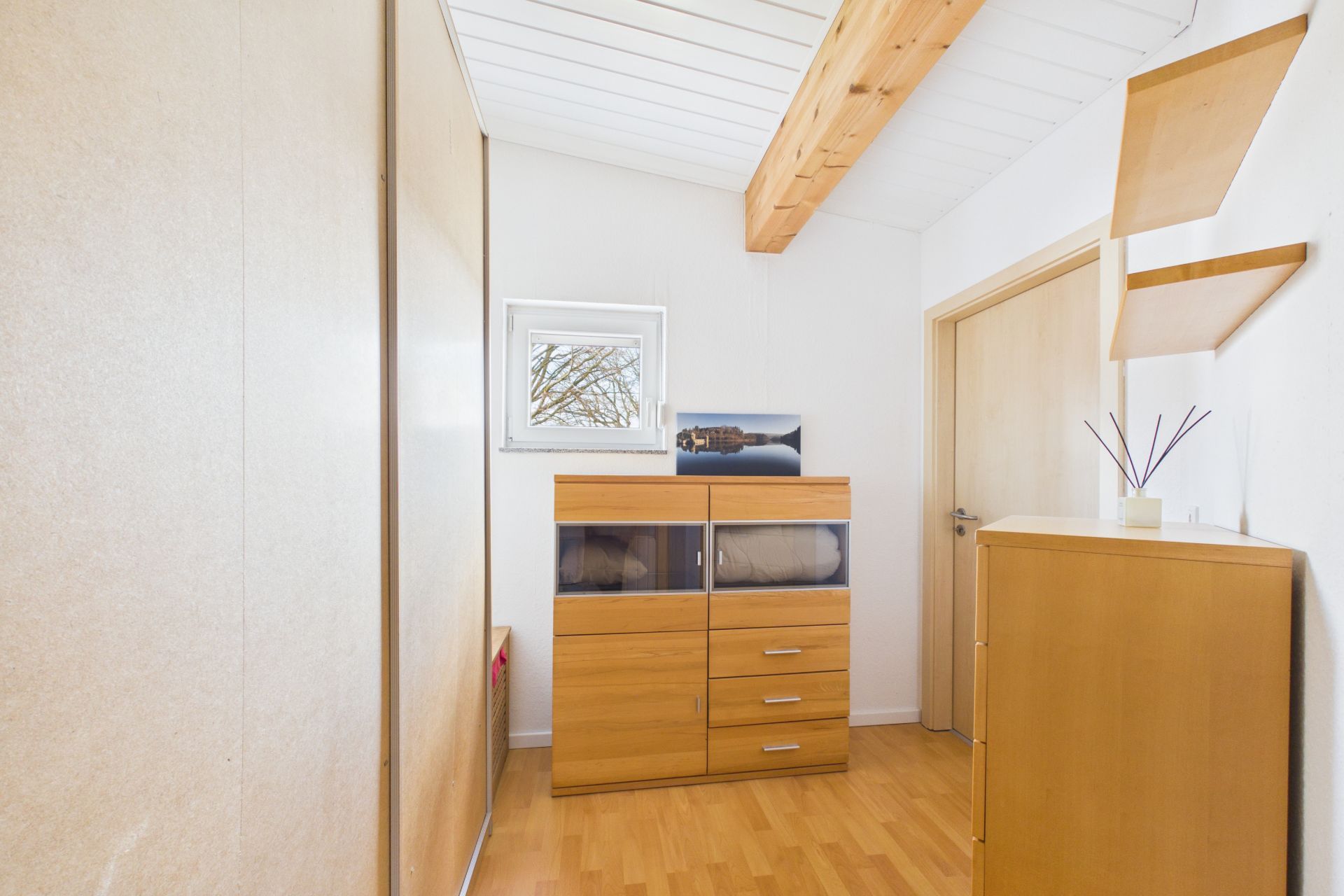 Heller Flur mit Holzschränken, Regal, kleinem Fenster und Holzbalken an der Decke.