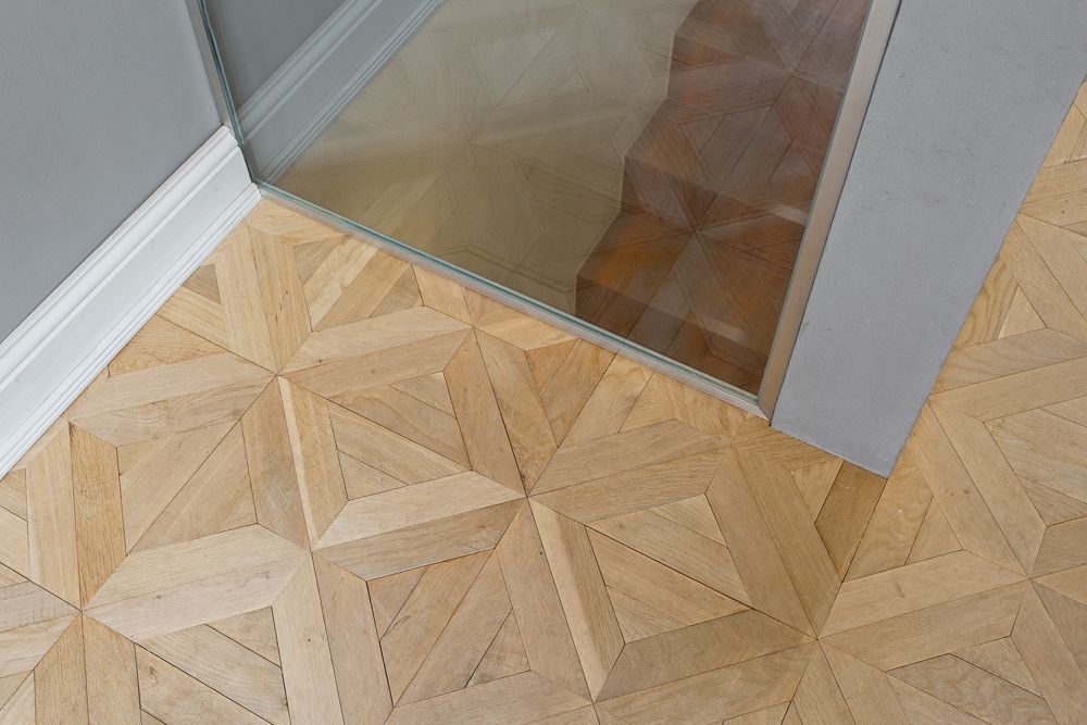 Heller Holzfußboden mit geometrischem Muster neben einer Glaswand und grauer Wand.
