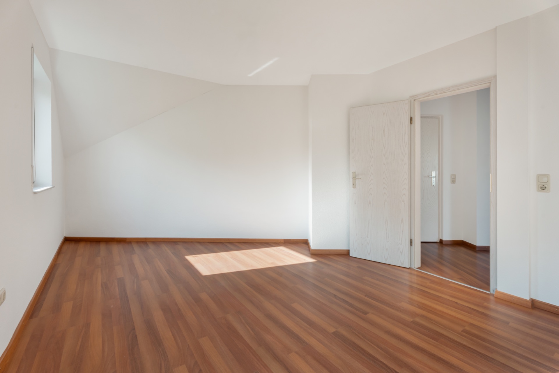 Leerer Raum mit Holzfußboden, weißer Wand, Fenster und geöffneter Tür.