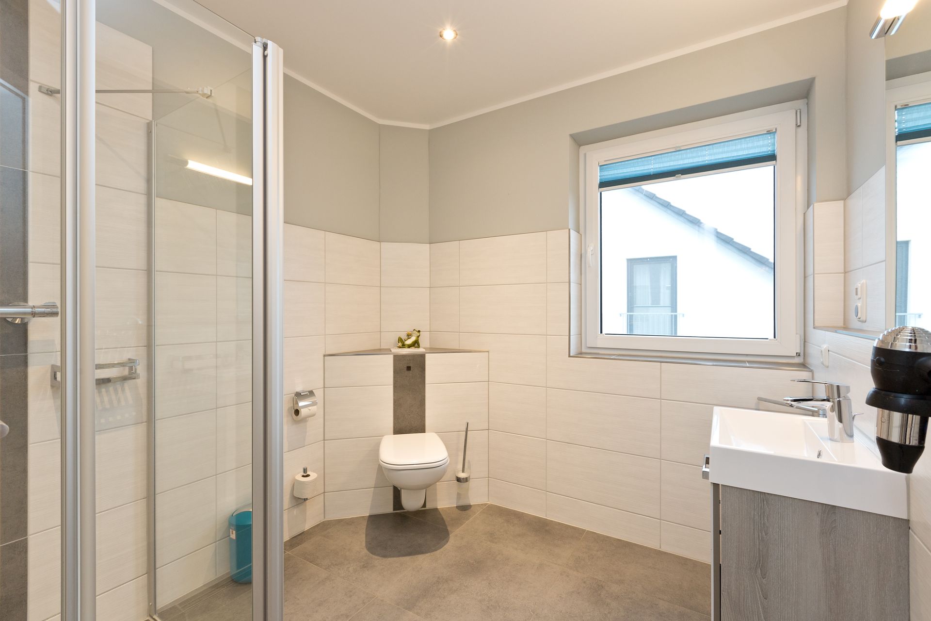 Modernes, helles Badezimmer mit bodengleicher Dusche, WC, Fenster und Waschbecken.