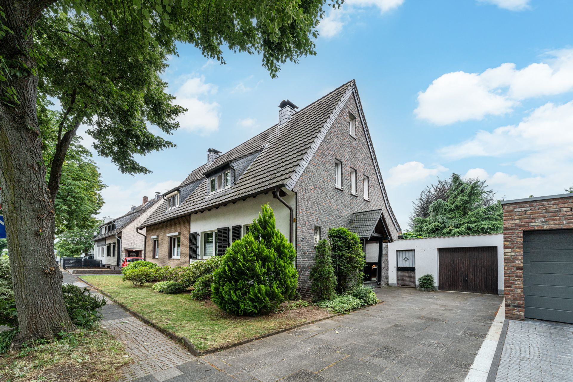 Zweistöckiges Wohnhaus mit Vorgarten, Auffahrt und angrenzender Garage.