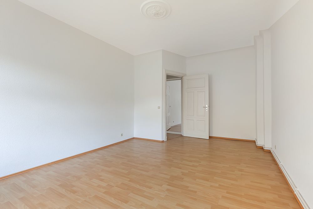 Leerer Raum mit hellem Holzboden, weißen Wänden und offener Tür.