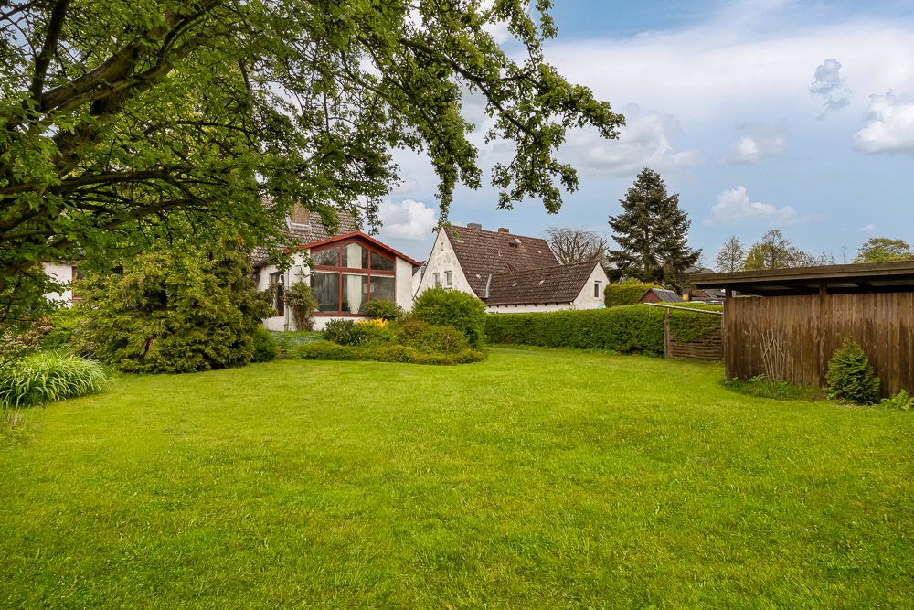 Großer, grüner Garten mit Bäumen, Blick auf ein Wohnhaus und einen Holzschuppen.