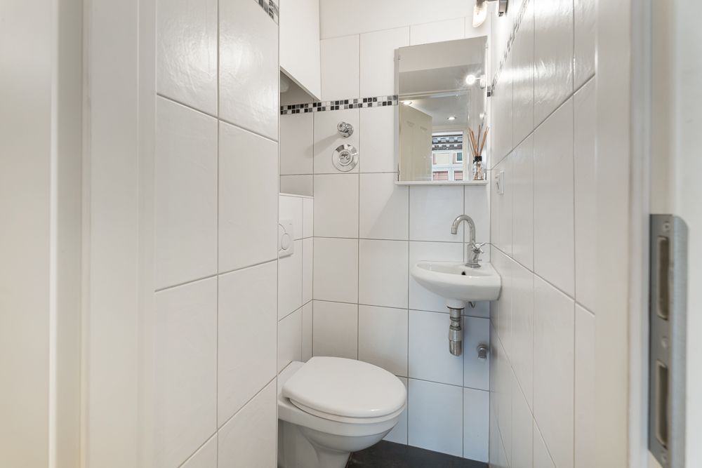 Kleines Badezimmer mit Toilette, Waschbecken und Spiegel, weiße Fliesen an den Wänden.