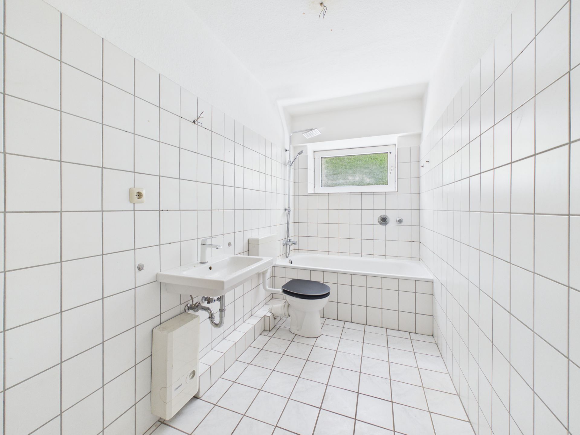 Weiß gefliestes Badezimmer mit Badewanne, Waschbecken, WC und Fenster.
