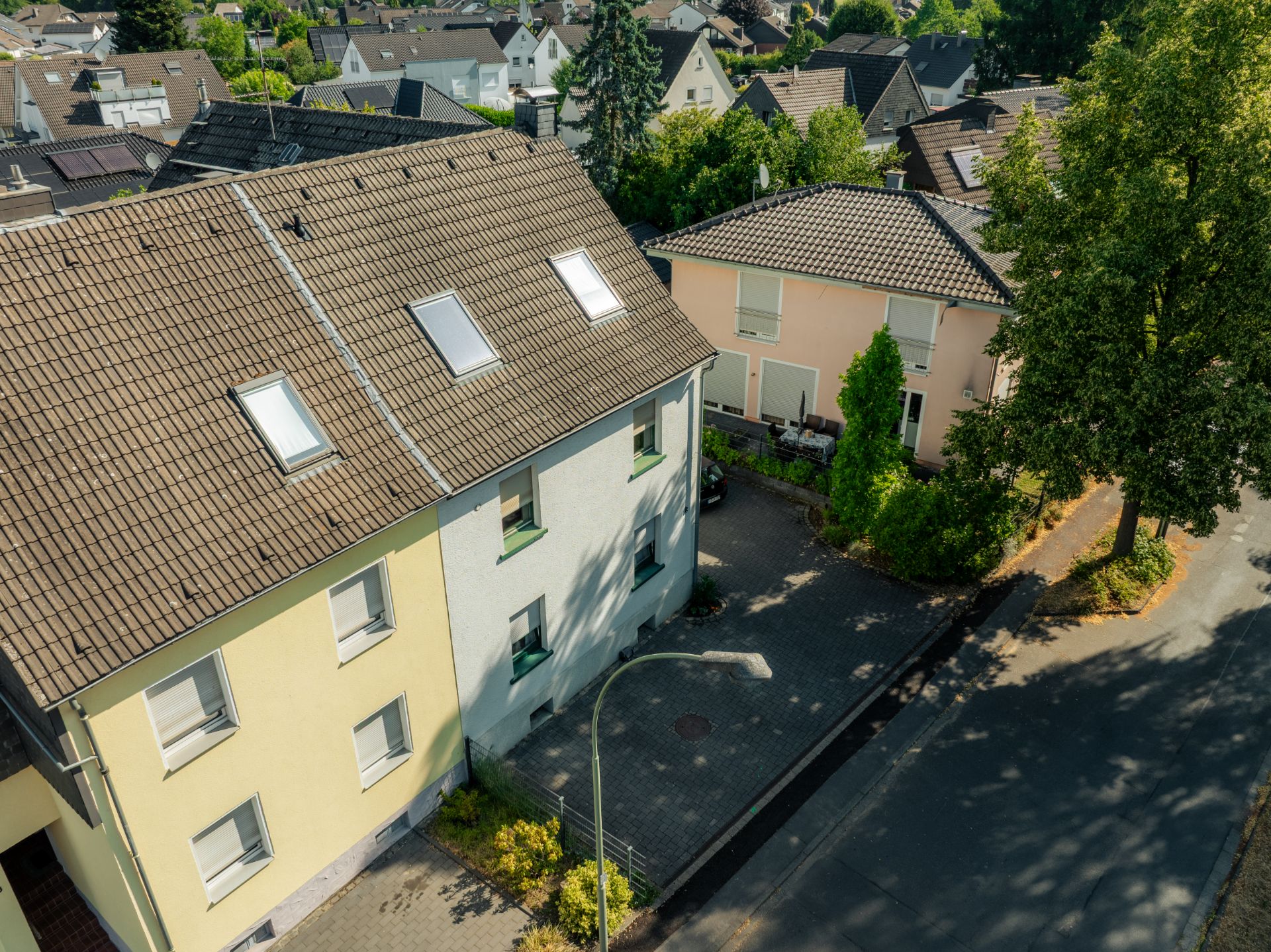 Mehrfamilienhaus mit Dachfenstern und Vorgarten an einer ruhigen Straße.