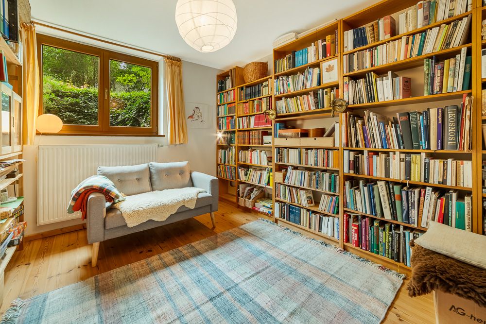 Helles Wohnzimmer mit Bücherregalen, kleinem Sofa, Teppich und großem Fenster.