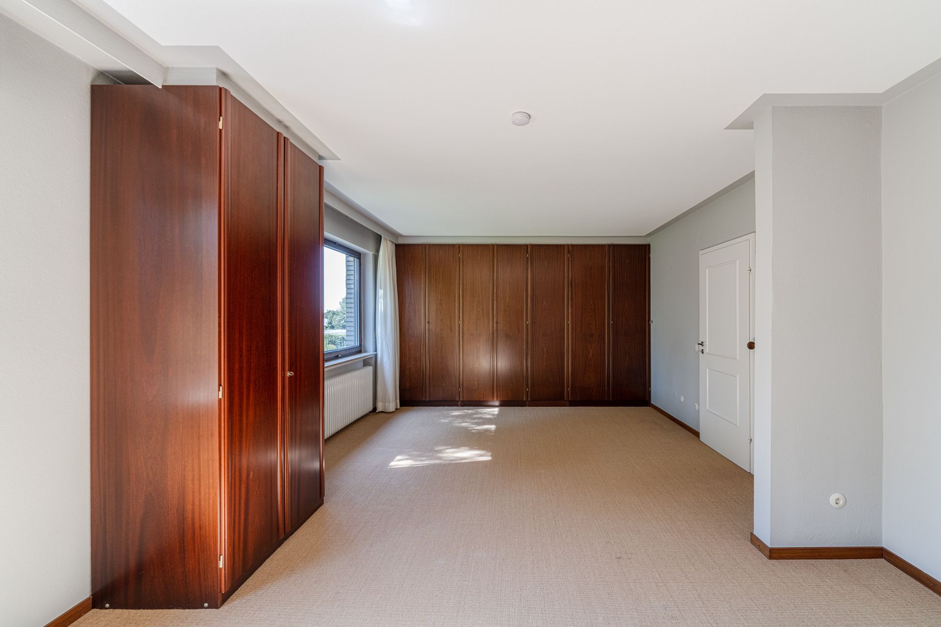 Leeres Zimmer mit großen Einbauschränken aus Holz, Fenster und weißer Tür.