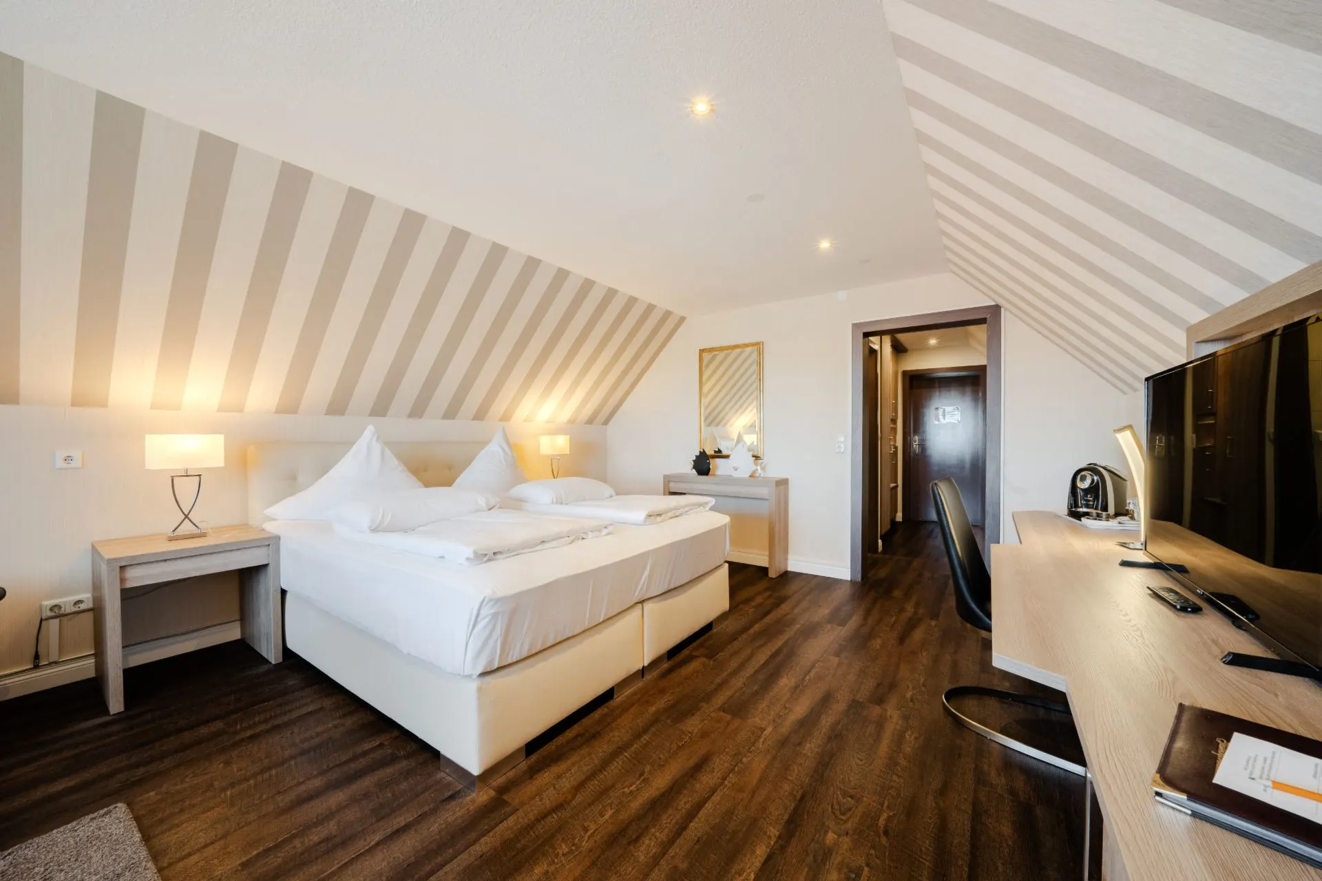 Modernes Schlafzimmer mit Doppelbett, Schreibtisch, Fernseher und Holzfußboden unter Dachschrägen.