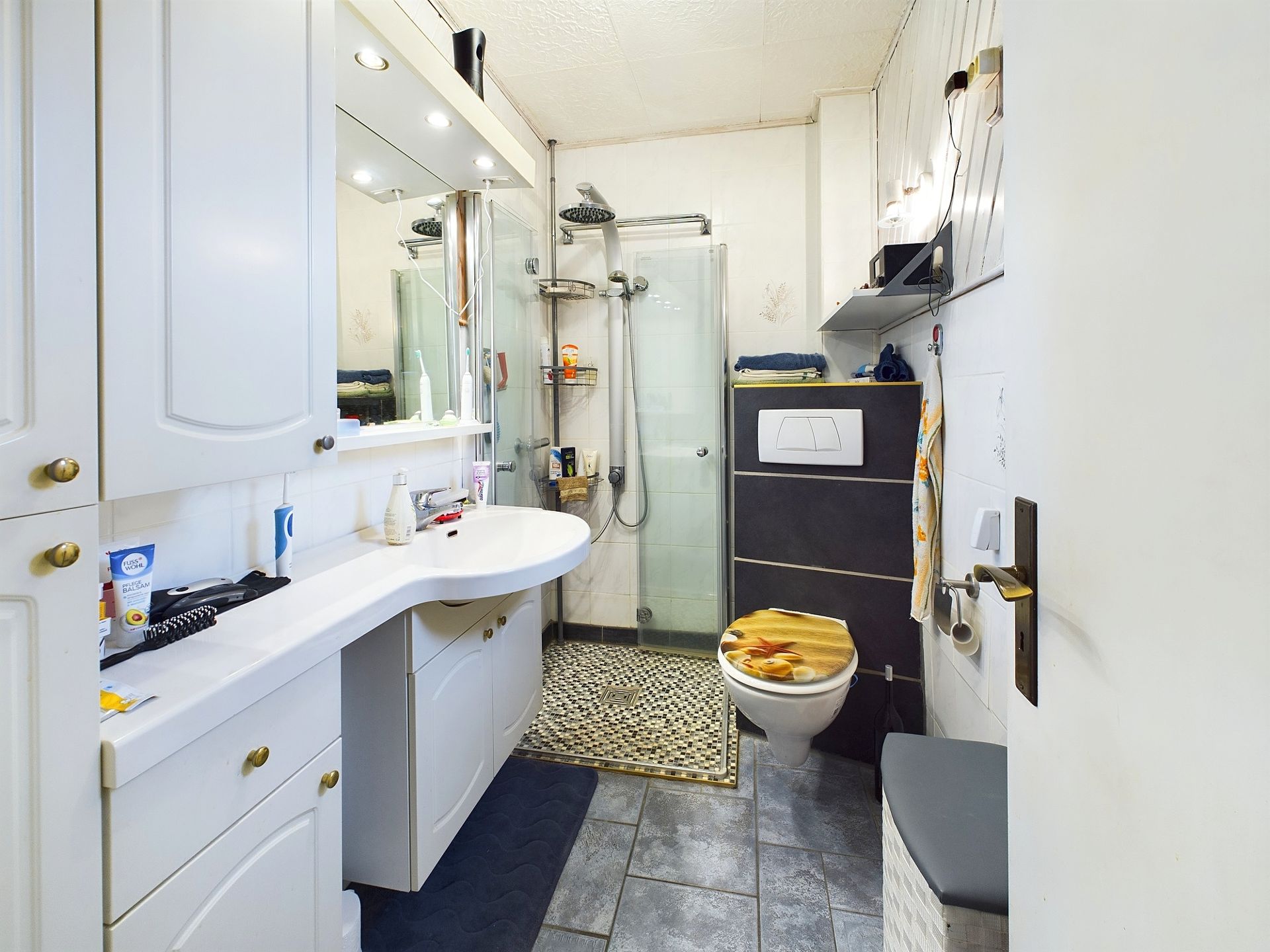Modernes Badezimmer mit Dusche, Waschbecken, Spiegel und WC, weiße Möbel und Fliesen.