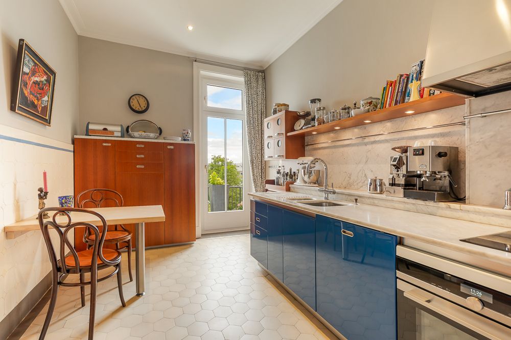 Helle Küche mit blauem Unterschrank, Holzmöbeln, kleinem Esstisch und Zugang zum Balkon.