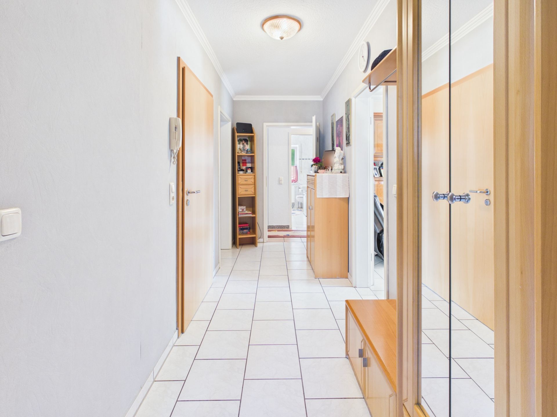 Heller Flur mit Fliesenboden, Holzmöbeln und Spiegel in einem Wohnhaus.