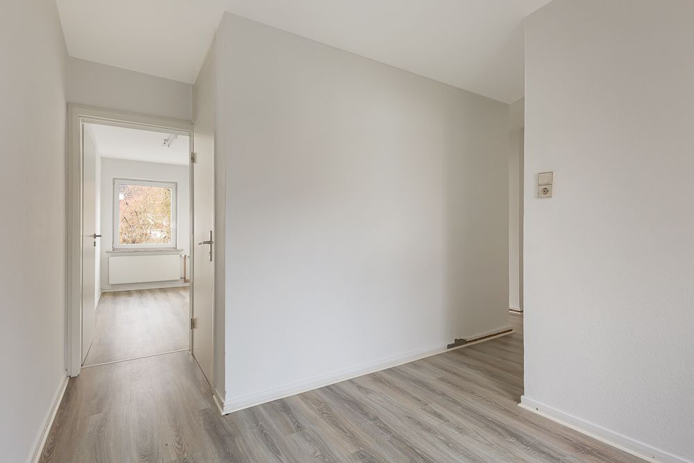Heller Flur mit Laminatboden, Türen zu weiteren Räumen und einem Fenster im Hintergrund.
