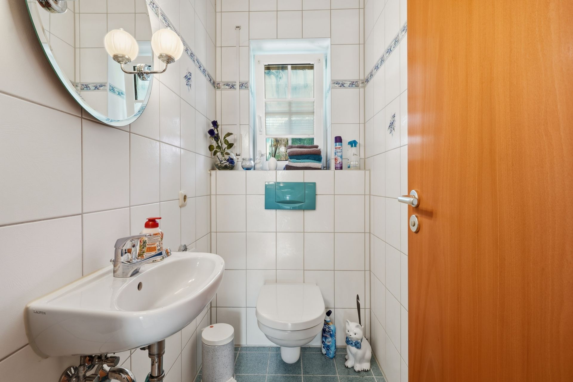 Kleines Bad mit WC, Waschbecken, Spiegel, Fenster und Dekorationen.