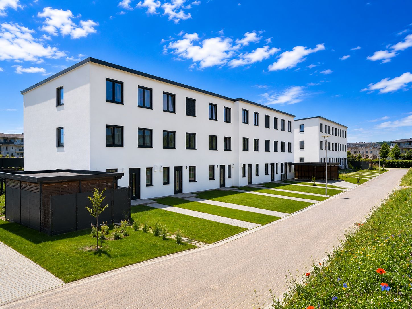 Moderne, weiße Wohngebäude mit drei Etagen und gepflegten Vorgärten an einer ruhigen Straße.