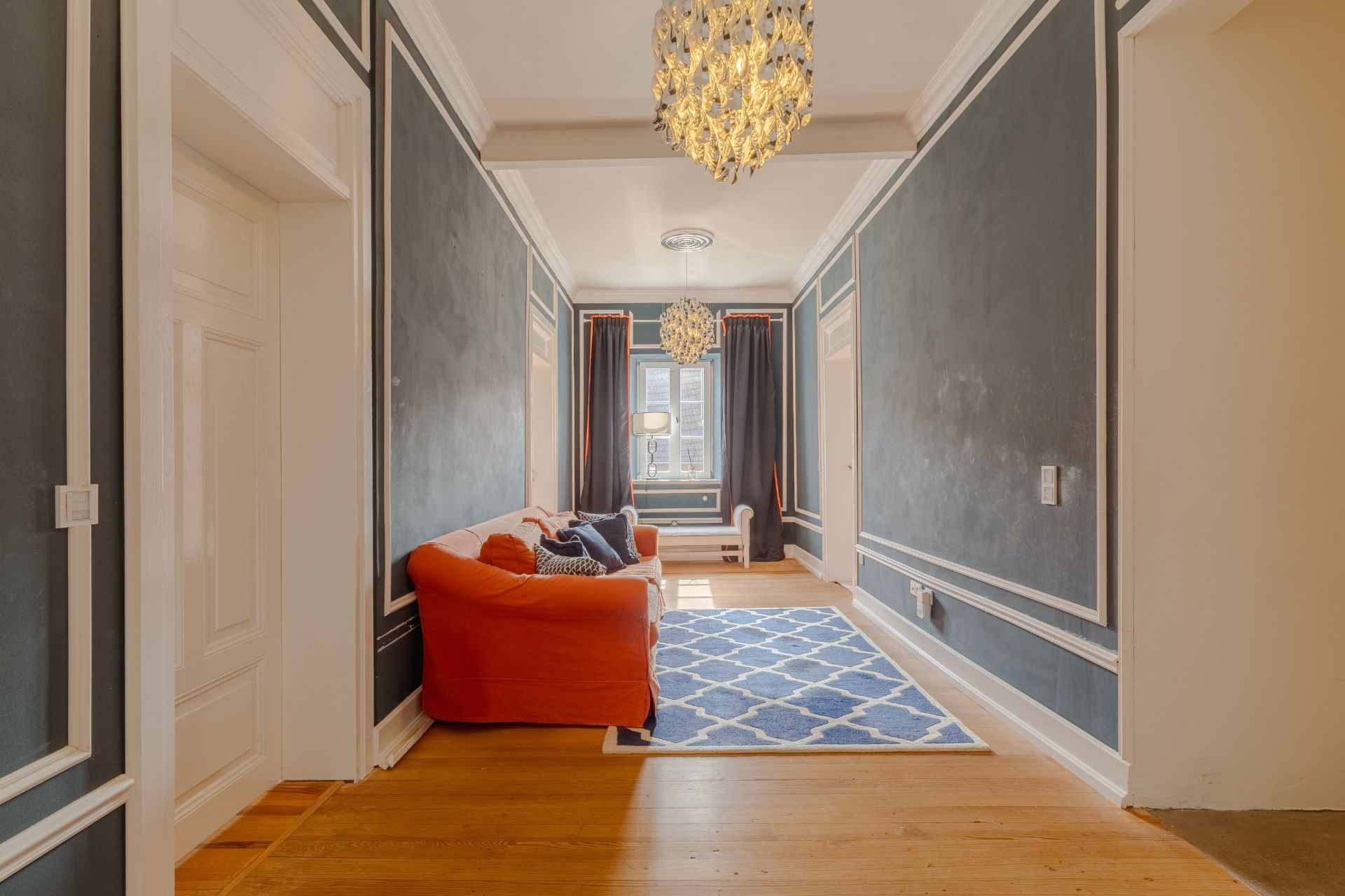 Wohnzimmer mit orangefarbenem Sofa, blauem Teppich und Kronleuchtern.