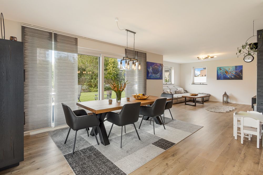 Helles Ess- und Wohnzimmer mit Holzboden, großem Tisch, Stühlen und Zugang zum Garten.
