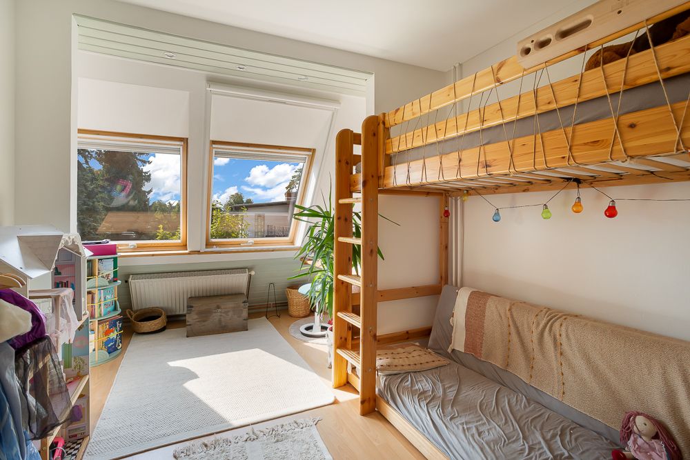 Helles Kinderzimmer mit Hochbett, großen Fenstern, Teppich und Pflanzen.