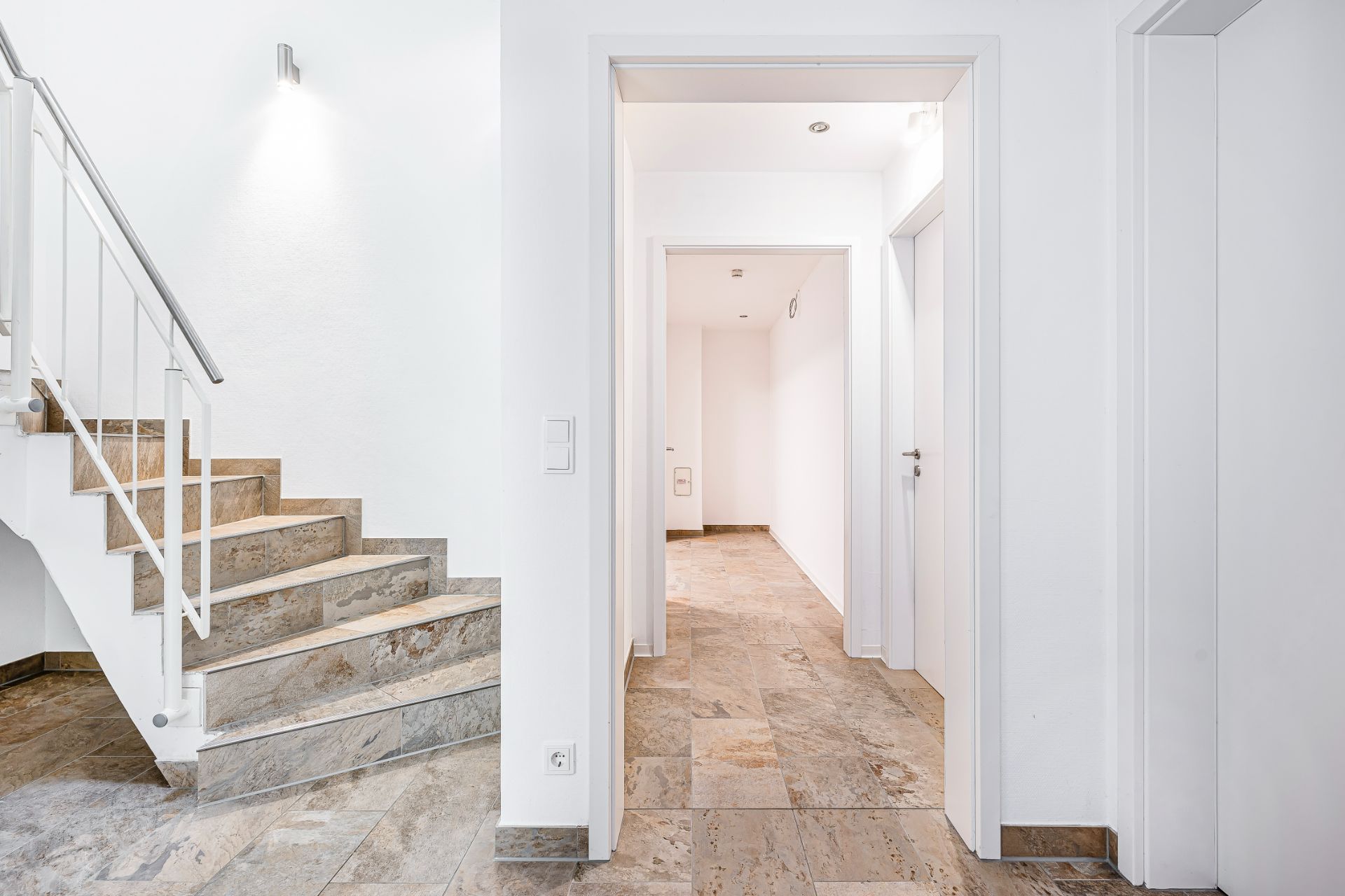 Heller Flur mit Steintreppe, mehreren Türen und Steinboden in einem Wohnhaus.