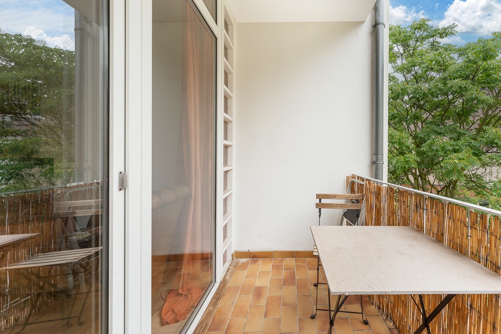 Balkon mit braunen Fliesen, Tisch, zwei Stühlen und Bambusverkleidung am Geländer.