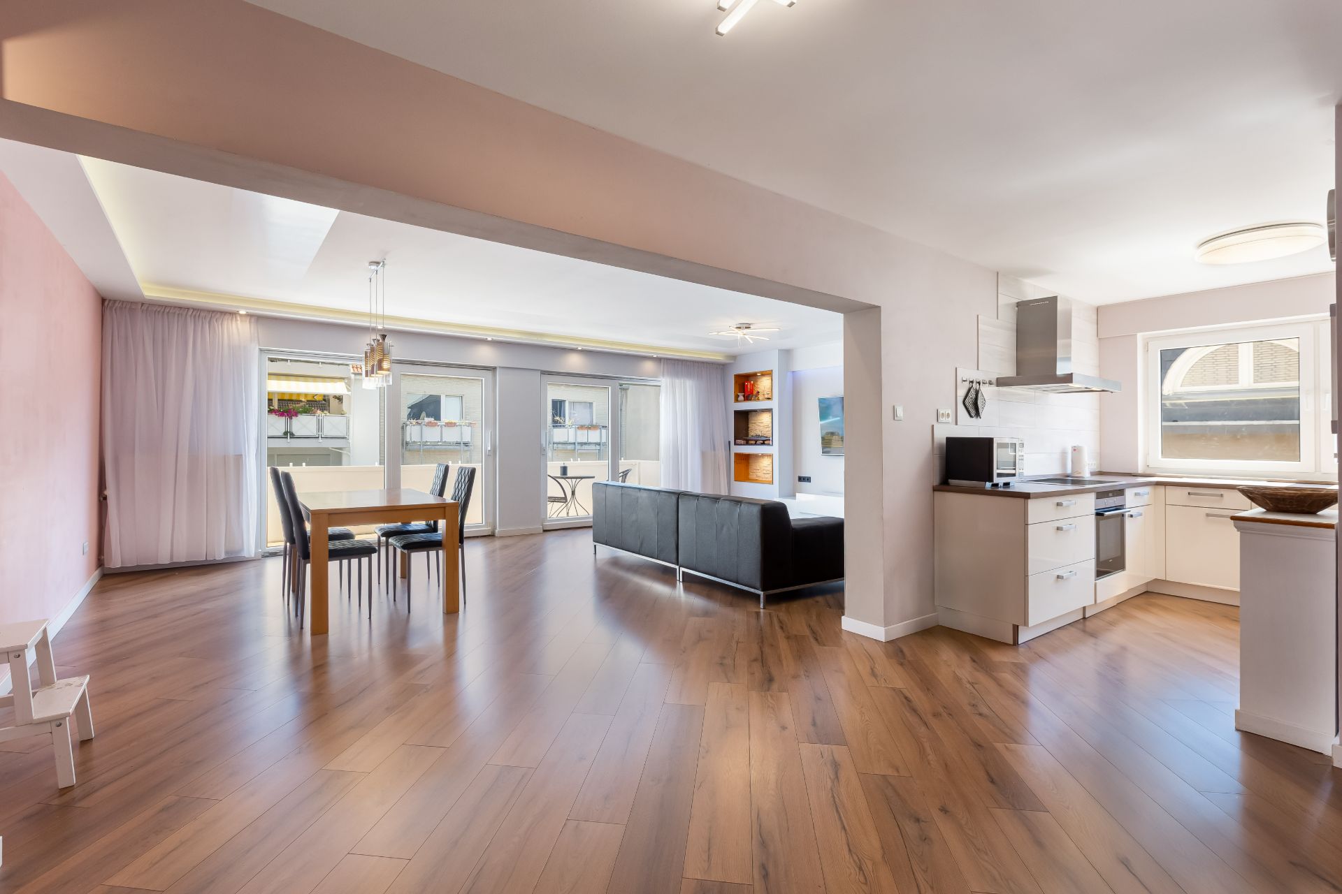 Helles Wohnzimmer mit offener Küche, Esstisch, Sofa und großen Fenstern mit Blick nach draußen.