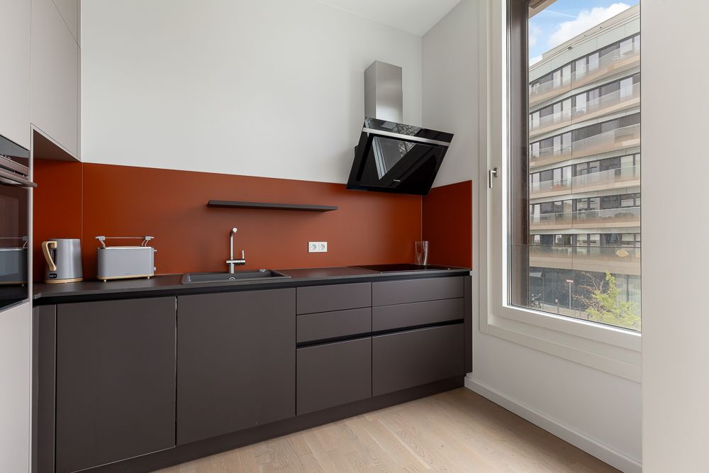 Moderne Küche mit dunklen Schränken, roter Rückwand und großem Fenster.