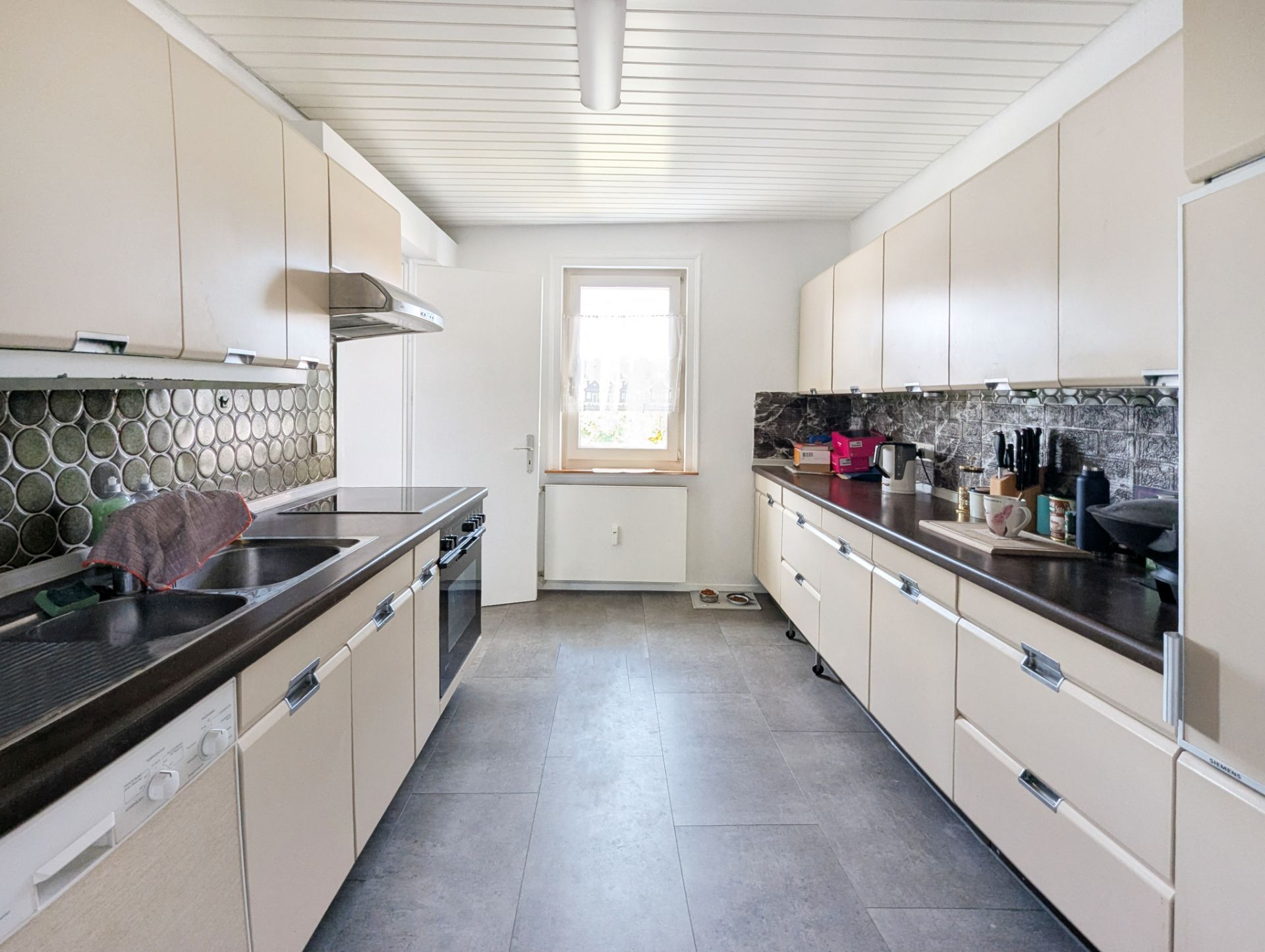 Helle, moderne Küche mit zwei langen Arbeitsflächen, Schränken und Fenster am Ende des Raums.