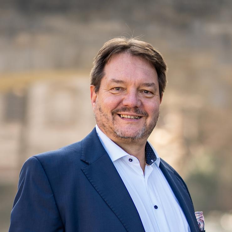 Ein Mann im blauen Anzug steht draußen und lächelt in die Kamera.