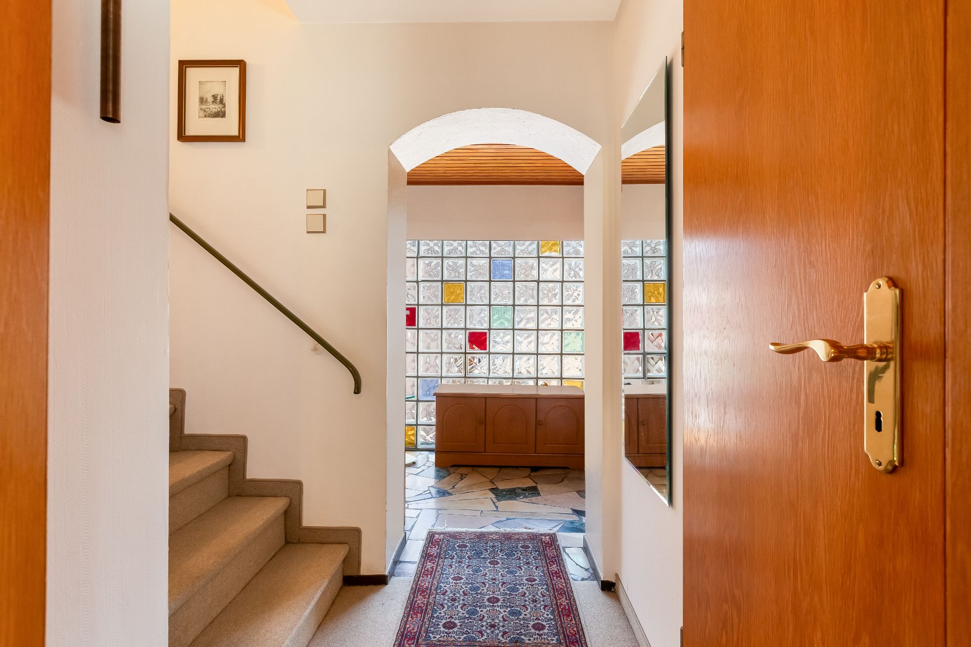 Heller Flur mit Teppich, Treppe links und Glasmauer im Hintergrund.