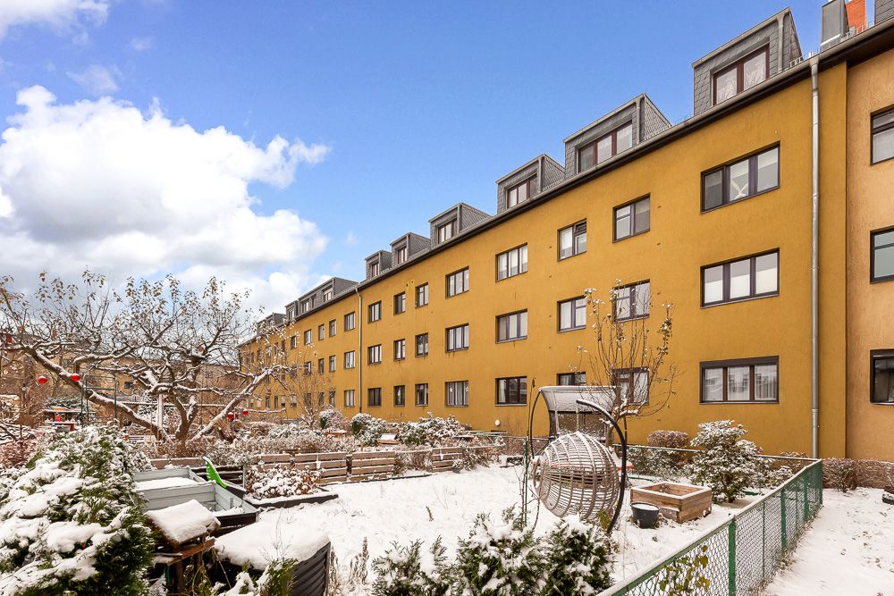 Gelbes Wohnhaus mit mehreren Fenstern und verschneitem Gemeinschaftsgarten im Vordergrund.