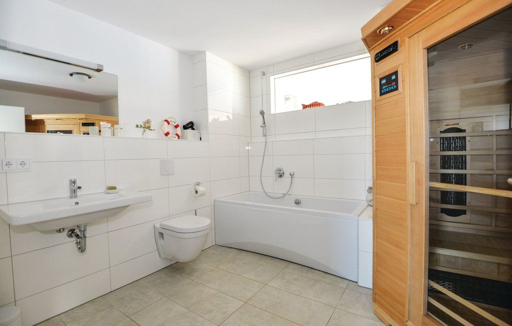 Modernes Bad mit Badewanne, Waschbecken, WC und einer Sauna, weiße Fliesen und großes Fenster.