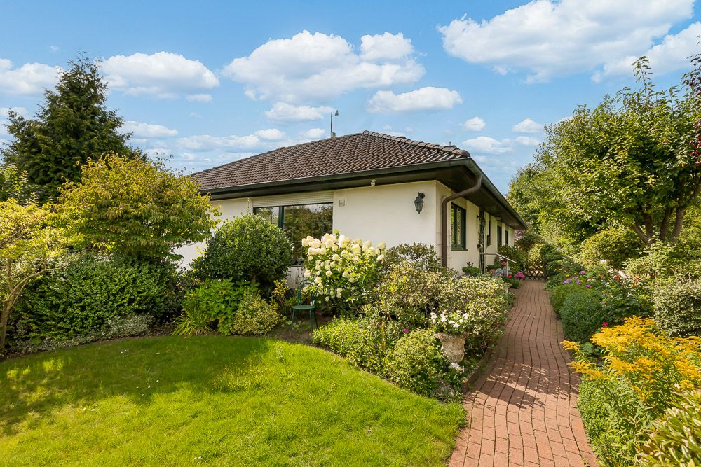 Einfamilienhaus mit gepflegtem Garten, Blumenbeeten und gepflastertem Weg bei Sonnenschein.