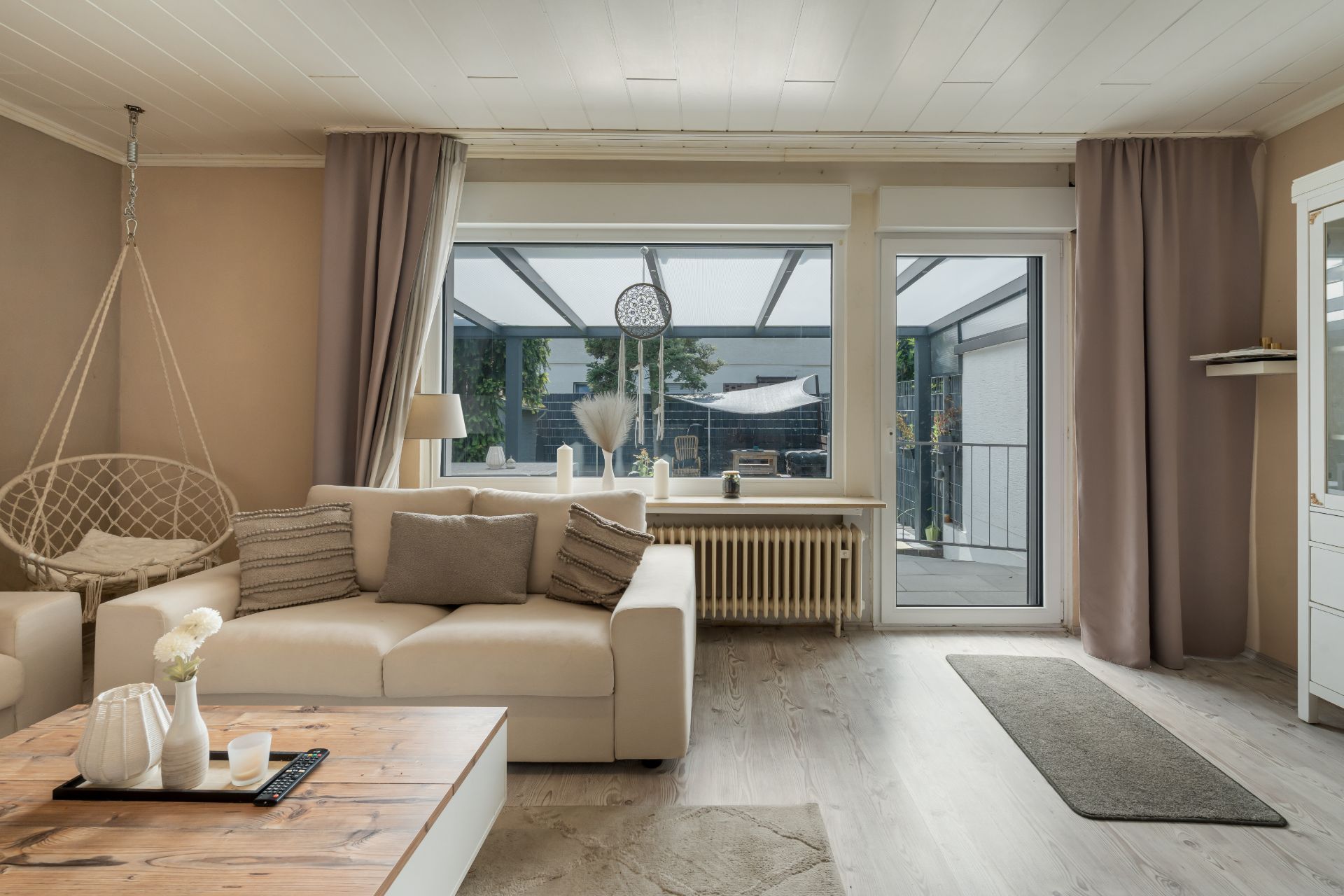 Helles Wohnzimmer mit Sofa, Hängesessel, Couchtisch und großem Fenster zur Terrasse.