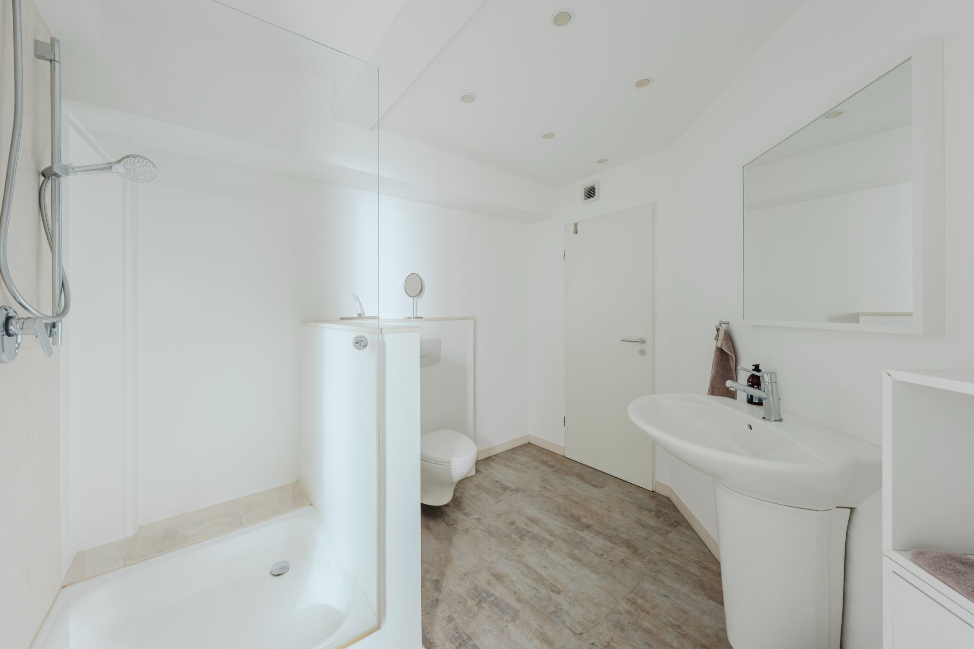 Modernes, weißes Badezimmer mit Dusche, Waschbecken, WC und Spiegel.