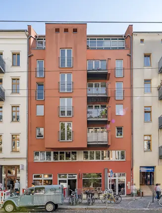 Mehrstöckiges Wohnhaus mit roten und beigen Fassaden, Balkonen und Fahrrädern davor.