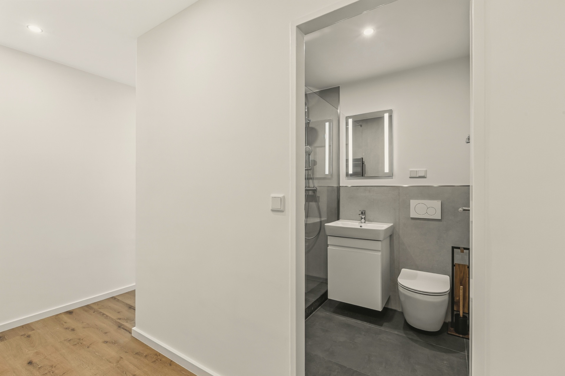 Modernes Bad mit WC, Waschbecken und Spiegel, Flur mit Holzfußboden davor.