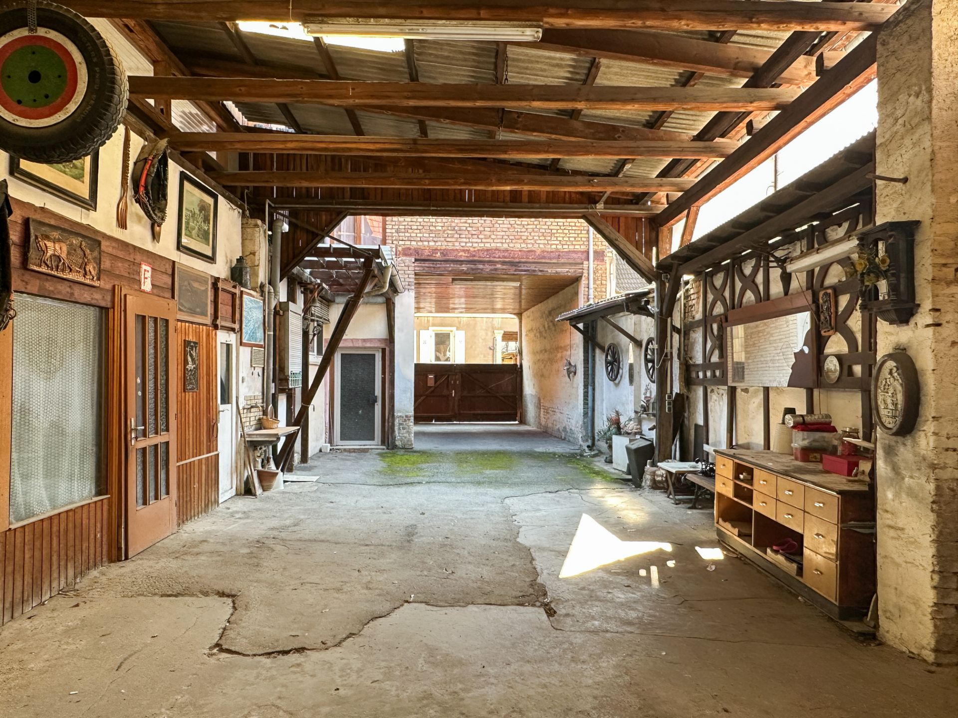 Überdachter Innenhof mit Holzbalken, Werkbank und Türen, Tageslicht fällt herein.