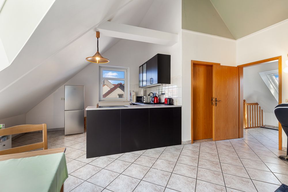 Moderne Küche mit schwarzer Einrichtung, Dachschräge und Fliesenboden, Sicht auf Flur und Treppe.