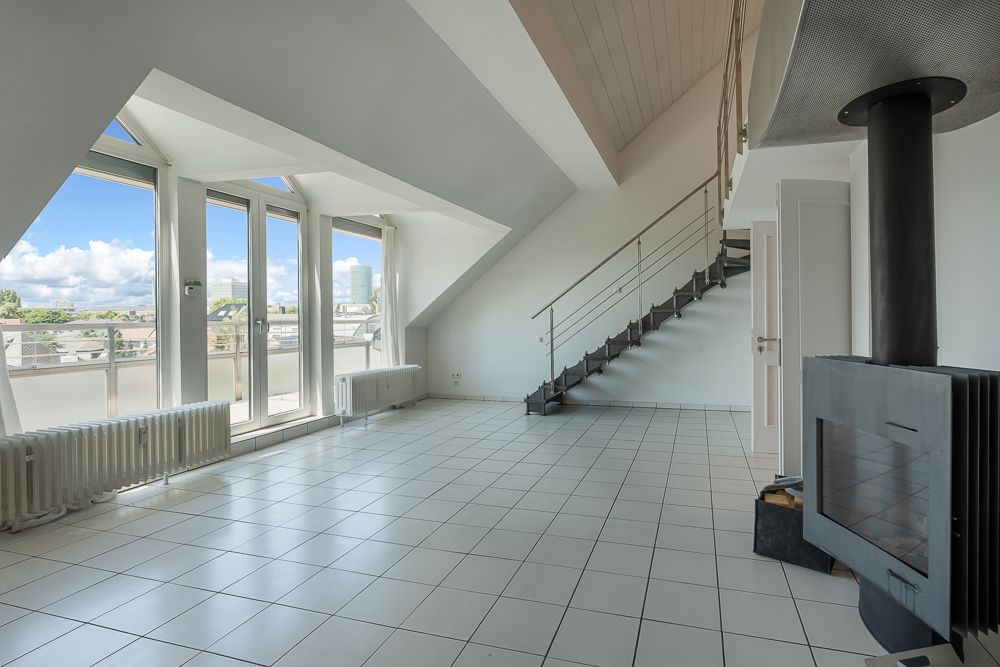 Helles Wohnzimmer mit Fliesenboden, Kamin, großen Fenstern und einer Treppe nach oben.