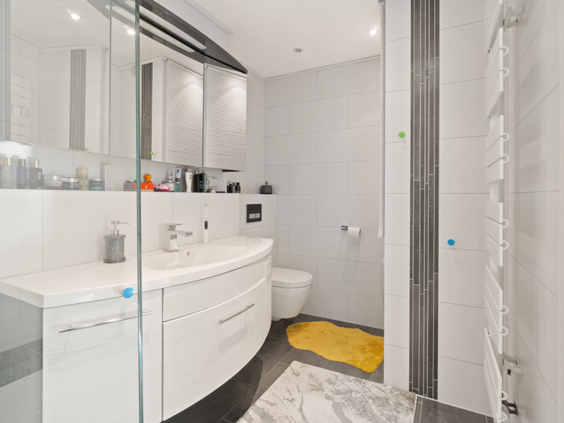Modernes Badezimmer mit weißem Waschtisch, Wandtoilette, Spiegel und gelbem Teppich.