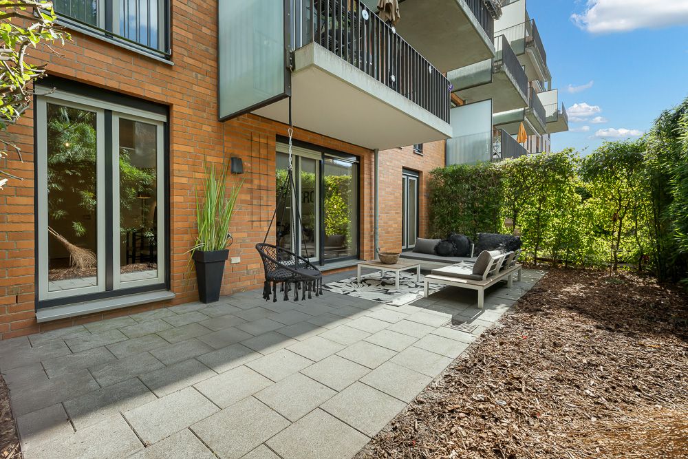 Moderne Terrasse mit Gartenmöbeln, Hängekorb und Pflanze vor einem Wohngebäude.