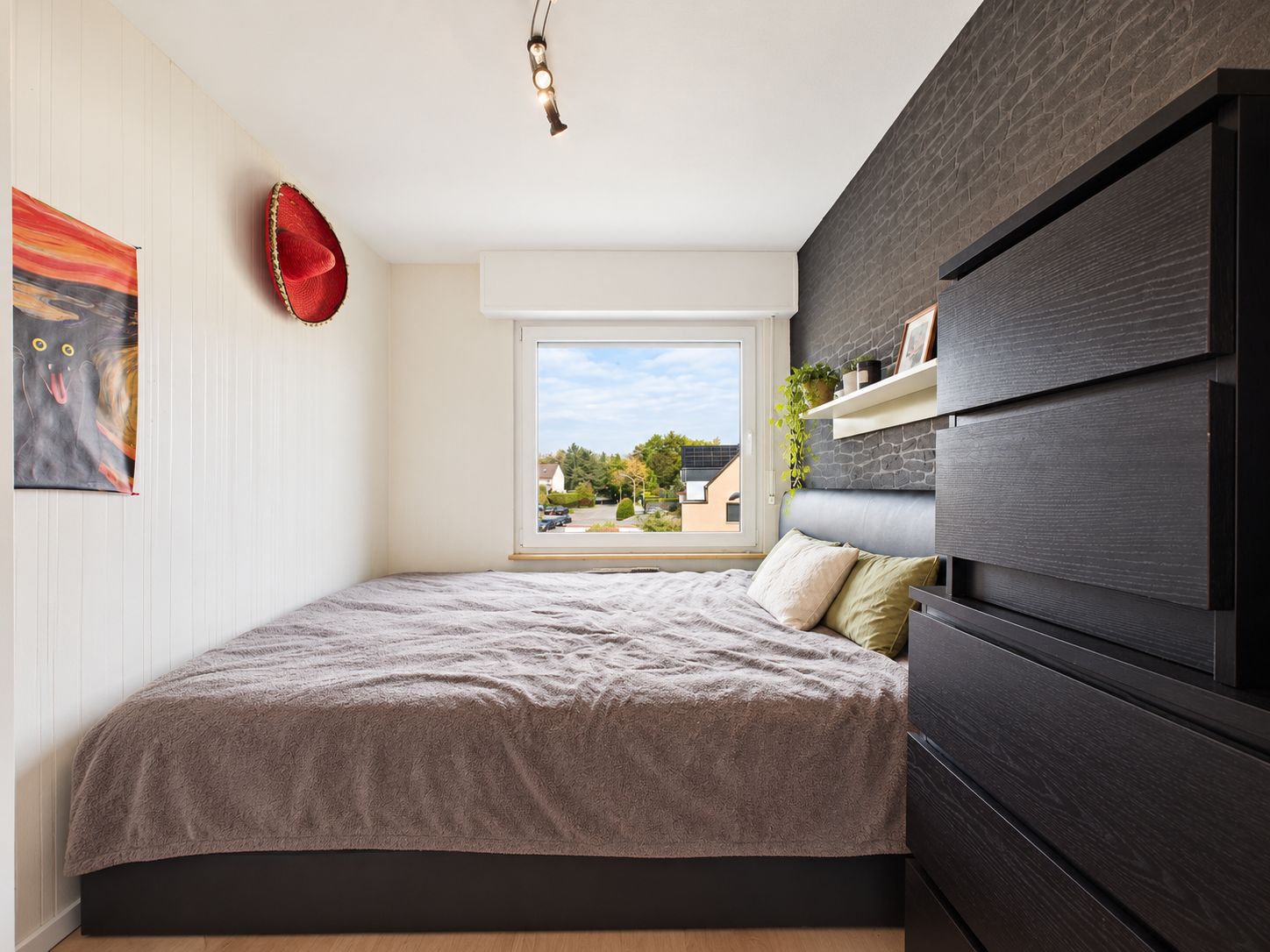 Kleines Schlafzimmer mit Doppelbett, Kommode, Regal und Fenster mit Blick nach draußen.